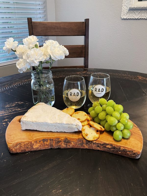 Image of stemless wine glasses with the RAD logo in white next to a cheese and cracker platter and vase with white flowers