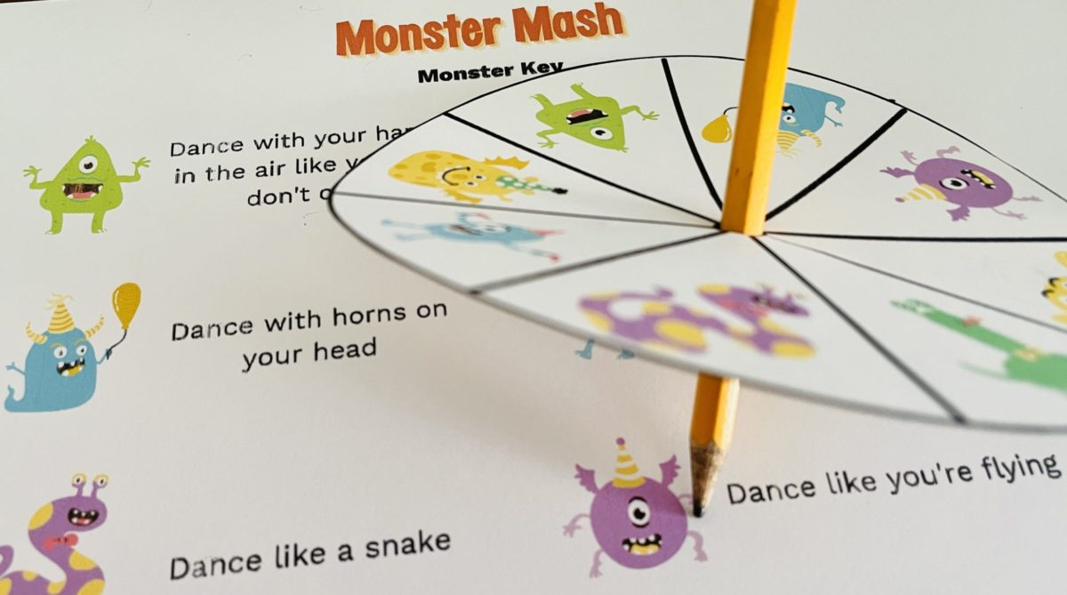 Pieces of the Monster Mash Game: A pencil poked through paper cut out in a circle with cartoon monsters on it. The spinner is resting on top of the Monster Key that has the pictures of the monsters along with dance moves.
