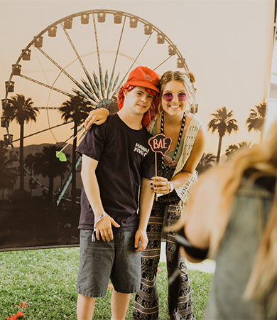 A young man and girl posing for a picture infront of a ferris wheel backdrop.