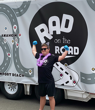 A man flexing his muscles in front of RAD on the Road truck.
