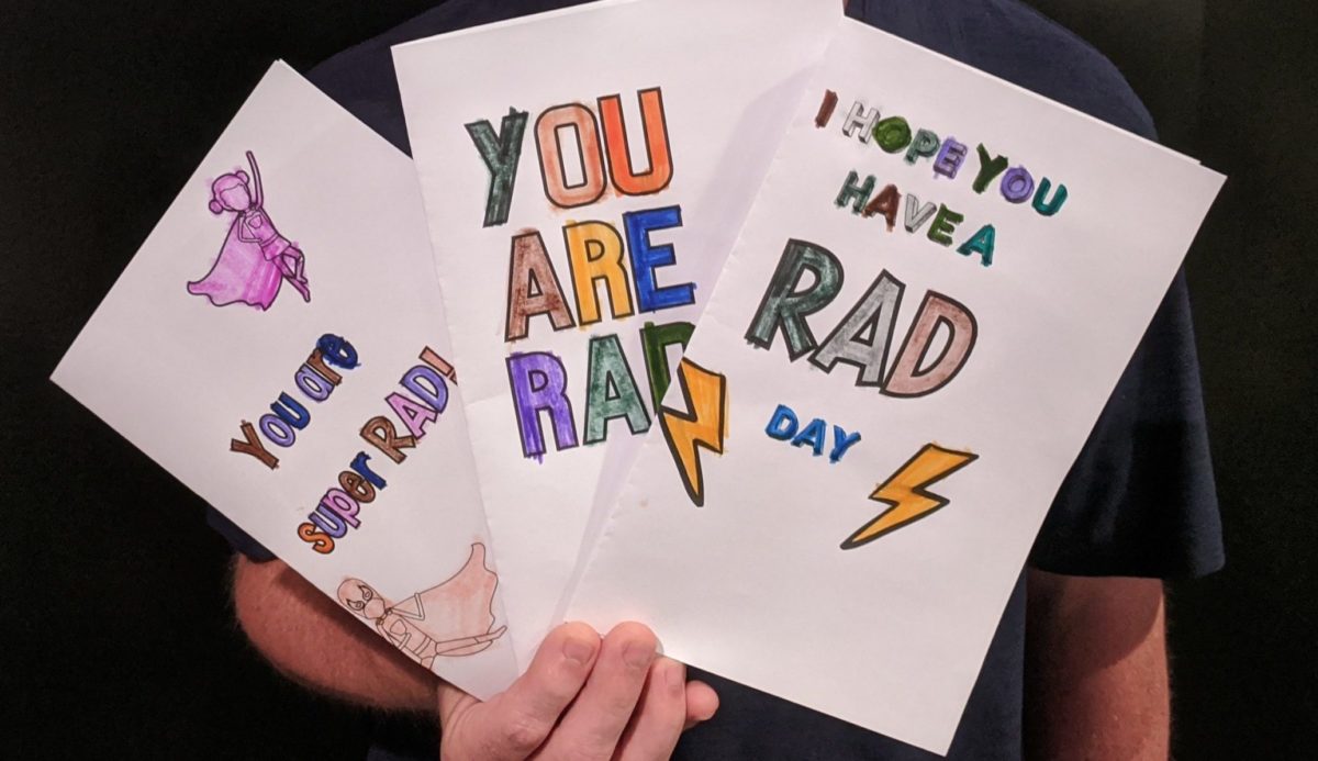 A person holding up 3 colored in cards that have RAD messages on them