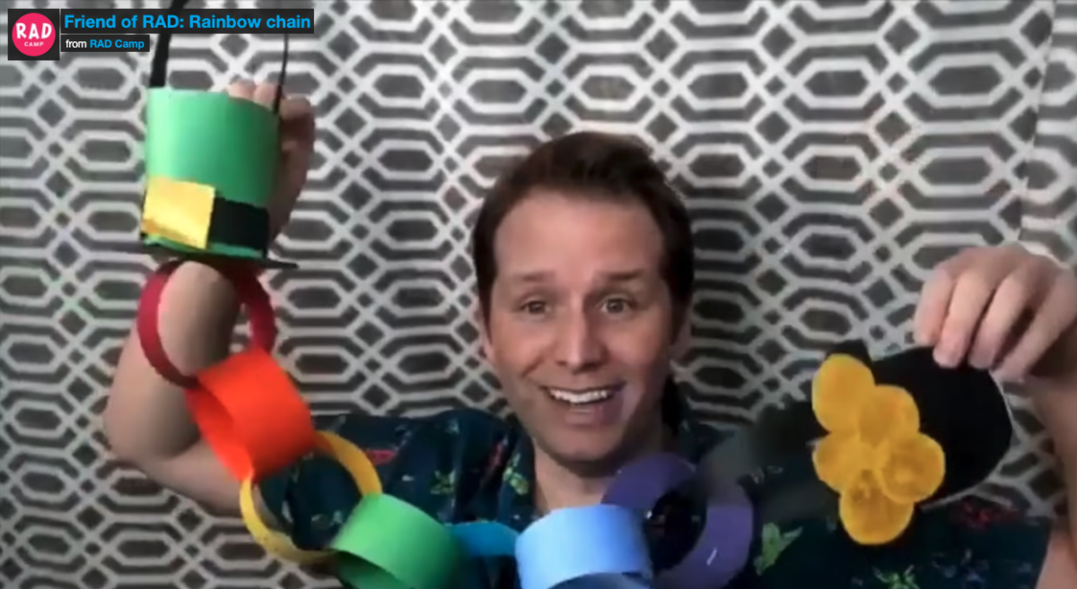 A man smiling and holding up a rainbow chain craft project