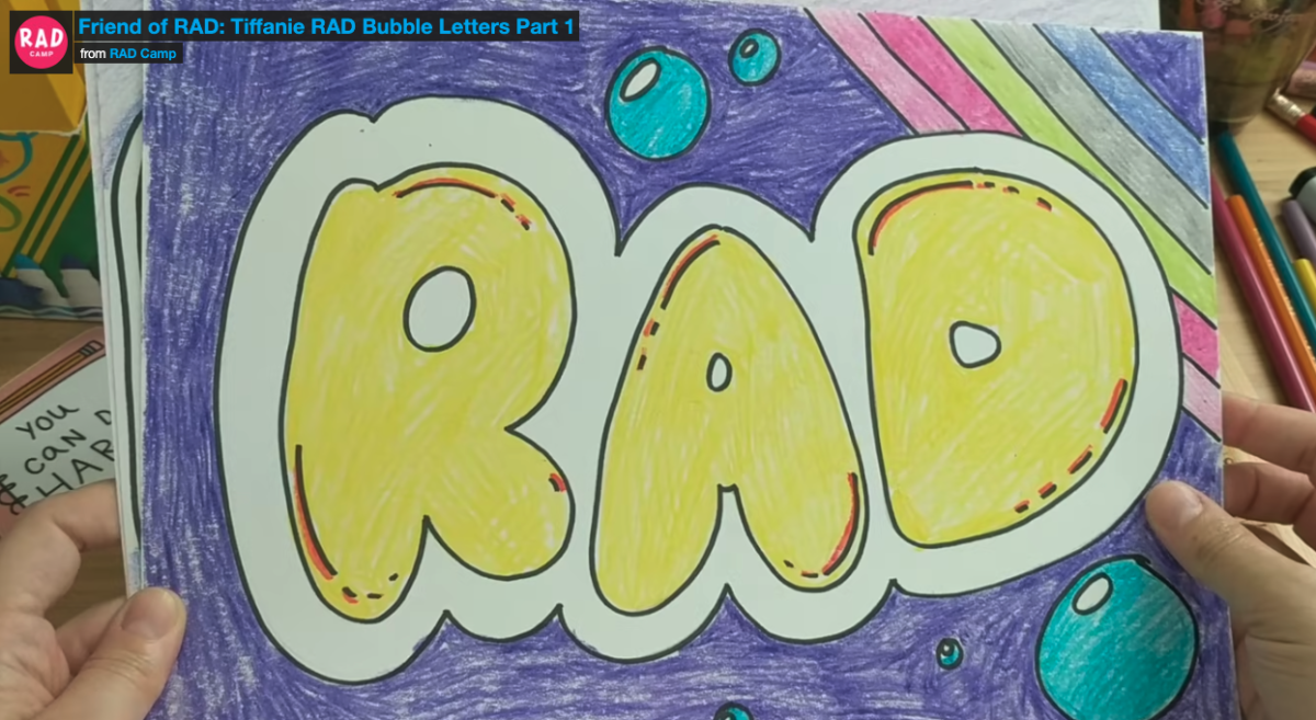Someone holding up a drawing of the words RAD in bubble letters